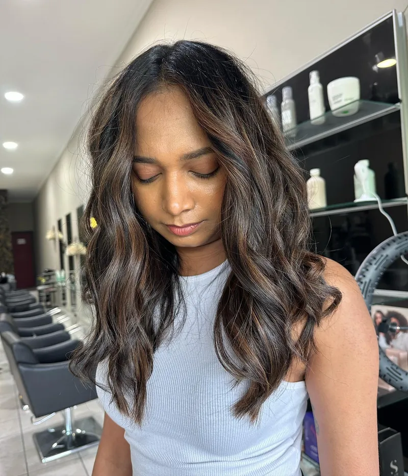 A client looking down at glossy, dark brown waves with caramel pieces
