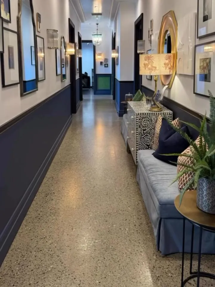 The hallway at Freedom Suites in Oakleigh: terrazzo floor, gallery wall, round brass mirror and a velvet sofa